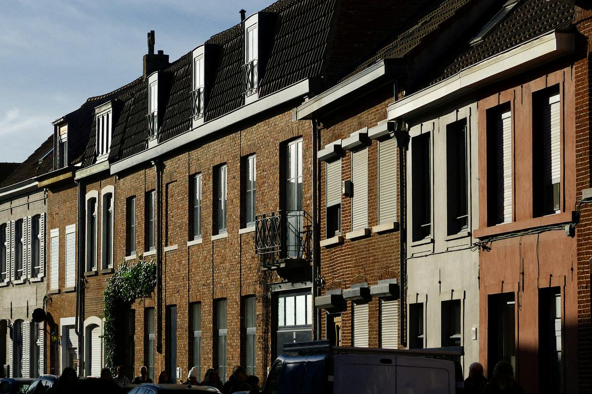 Een rij bakstenen rijwoningen met rolluiken en dakkapellen in een gewone straat.