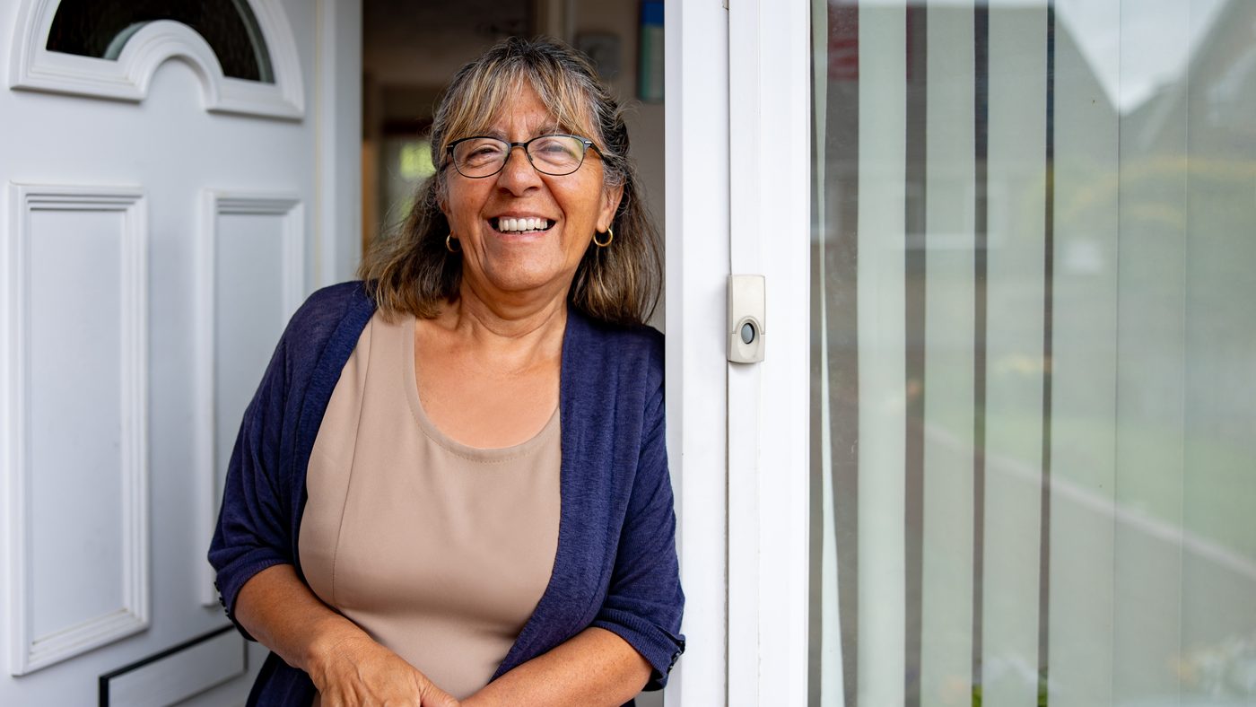 Een vrouw staat glimlachend in de open voordeur van haar woning.